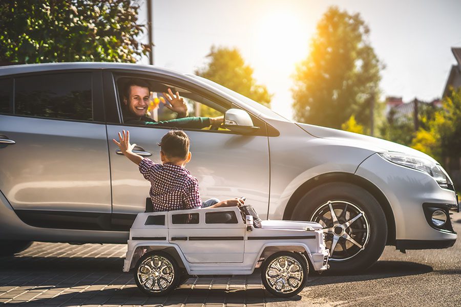 Blog - Smiling Father Driving In Car Waving To His Son In Electric Car Toy